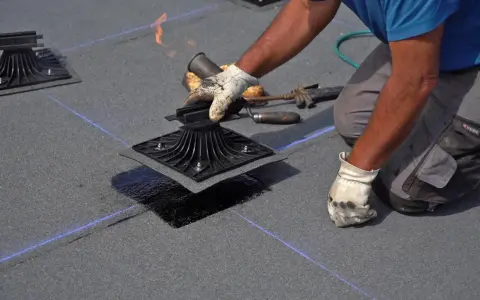 Instalador aplica calor con soplete para fijar tela asfáltica a base de techo, asegurando impermeabilización.