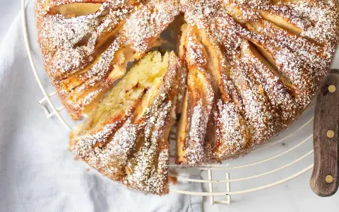Deliziosa torta di mele in friggitrice ad aria, cosparsa di zucchero a velo, con una fetta tagliata che mostra la morbidezza dell'interno.