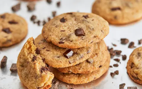 Ein Stapel saftiger american cookies mit Schokoladenstückchen, einer angeknabbert, umgeben von Schokoladenstückchen.