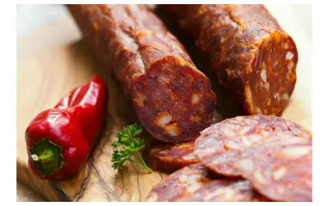 Kawałki pikantnego chorizo, czerwona papryczka i natka pietruszki na desce. Dowiedz się, chorizo co to jest!