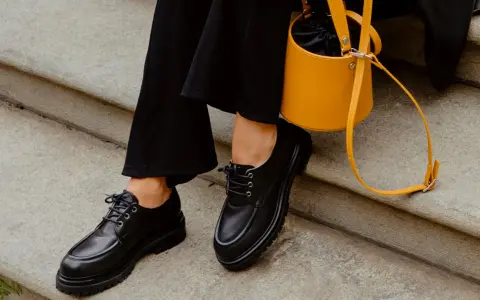 Come abbinare le stringate femminili: look audace con pantaloni neri e borsa gialla.