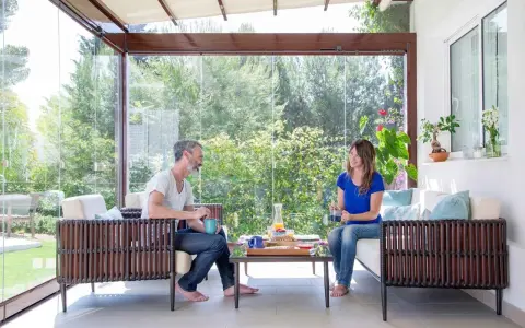 Pareja disfrutando de un café en un **porche acristalado** con vistas a un jardín exuberante.
