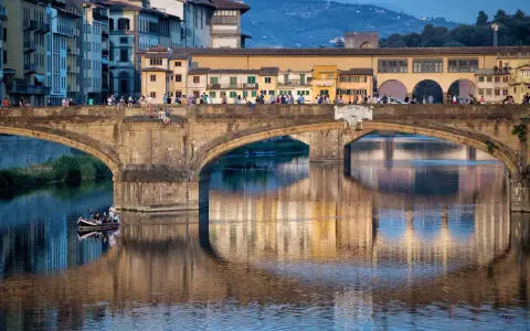 Le Ponte Vecchio à Florence, avec ses maisons colorées et ses reflets sur l'Arno. Une barque navigue paisiblement sous le pont.