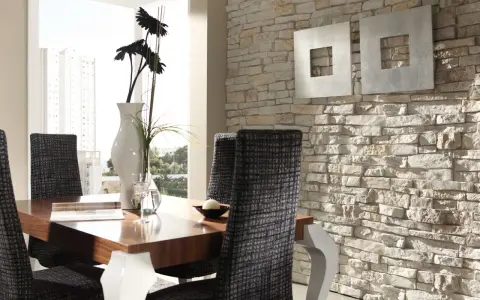 Comedor moderno con mesa de madera, sillas tapizadas y una pared con distintos tipos de revestimientos de piedra.