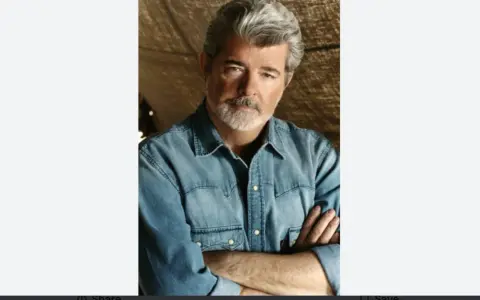 George Lucas, uno dei registi importanti, con barba grigia e camicia di jeans, braccia conserte.