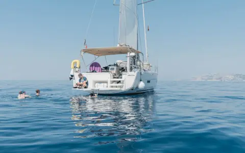 Erfahrungen, wenn du der Crew beitrittst: Ein Mann sitzt auf einer Yacht, während andere im Meer schwimmen.