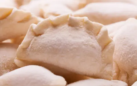 Zbliżenie na grupę surowych, mrożonych pierogów z widocznym, pofałdowanym brzegiem.