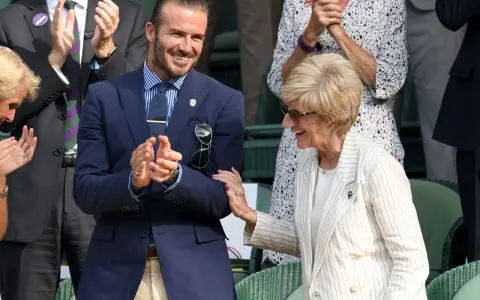Uomo con abito spezzato uomo giacca blu pantalone beige, sorride e applaude. Accanto a lui, una donna con giacca a righe.
