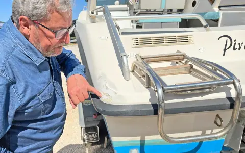 Un homme examine les dégâts sur le gelcoat d'un bateau. C'est quoi le gelcoat ? C'est la couche protectrice extérieure.