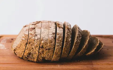Pokrojony bochenek ciemnego chleba na desce. Zastanawiasz się, ile kcal ma kromka chleba?