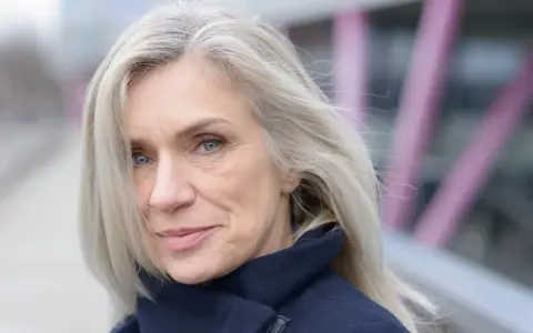 Donna con capelli bianchi e occhi azzurri, indossa un cappotto blu scuro. Un esempio di come vestirsi con i capelli bianchi.
