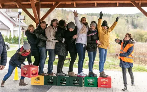 Uczestnicy zabawy, w ramach konkurencji sportowych dla dorosłych, tworzą łańcuch, balansując na skrzynkach po piwie.