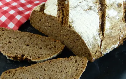 Ein rustikales tschechisches Brot, frisch aufgeschnitten, mit einer kräftigen Kruste und einer saftigen Krume. Daneben liegt eine rot-weiß karierte Serviette.