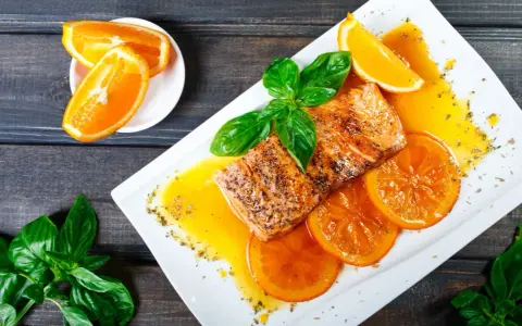 Delicioso salmón a la naranja, servido con rodajas de naranja y hojas de albahaca fresca.