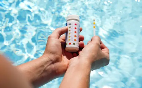 Hands hold a pool test strip and bottle, showing how to make pool water clear by checking chemical levels.