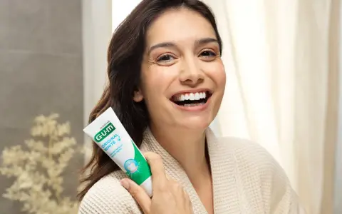 Uśmiechnięta kobieta trzymająca pastę GUM Original White. Dbanie o dziąsła (gum care) to klucz do pięknego uśmiechu.
