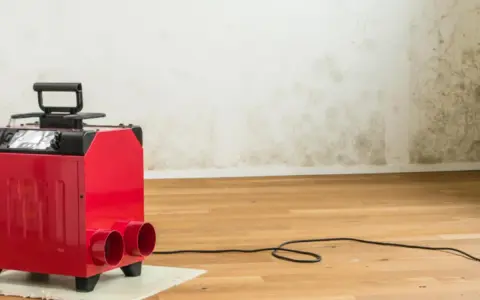 Roter Bautrockner im Einsatz gegen Wasserschaden. Die Wand zeigt deutliche Spuren von Feuchtigkeit und Schimmel.