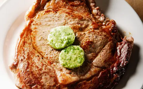 Un savoureux steak de bœuf, parfaitement grillé, est garni de deux rondelles de beurre maître d'hôtel, prêt à fondre.