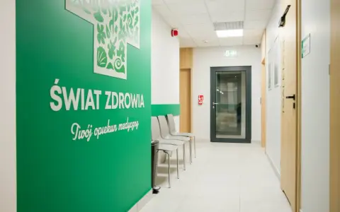 Zielona ściana z napisem "Świat Zdrowia" i logo, korytarz kliniki medycznej z drzwiami i krzesłami.