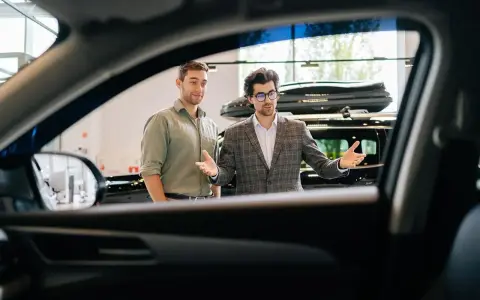 Dwóch mężczyzn w salonie samochodowym, jeden prezentuje auto.