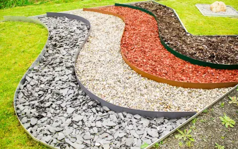 Geschwungene Beete mit verschiedenen Schichten aus grauem Schiefer, hellem Kies, roter Rindenmulch und dunklem Rindenmulch, die durch Metallkanten für rasenkanten setzen getrennt sind.