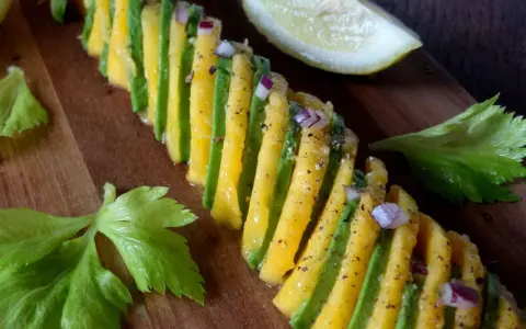 Une belle recette avocat et mangue, assaisonnée d'oignon rouge et de poivre, sur une planche en bois.