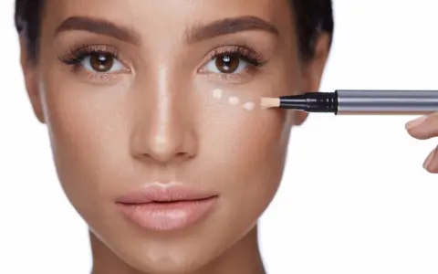Application de correcteur pour camoufler un cerne bleu. Le pinceau dépose des points de produit sous l'œil.