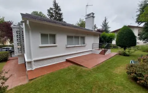 Terraza exterior con suelo de baldosas rojas recién pintado, rodeada de césped verde y un jardín frondoso.