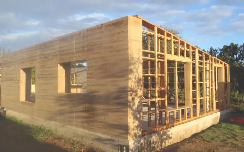 Construction d'une maison terre crue aux murs stratifiés, avec une ossature bois visible pour la suite.