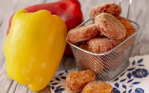 Polpette di peperoni dorate e croccanti, servite in un cestino, accanto a peperoni freschi rossi e gialli.