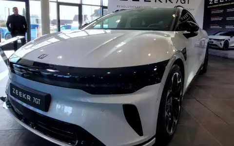 Ein Mann steht vor einem glänzenden, weißen Zeekr 7 GT in einem Ausstellungsraum. Das Auto hat eine markante schwarze Frontpartie.