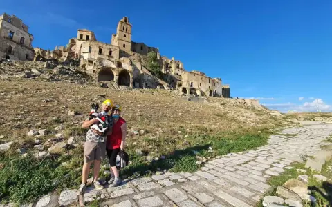 Coppia con cane visita le suggestive rovine di Craco vecchia, un borgo fantasma sotto un cielo azzurro.