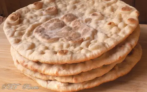 Una pila di pane naan senza lievito, dorato e soffice, su un tagliere di legno.