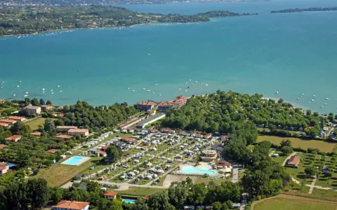 Widok z lotu ptaka na camping Baia Verde nad turkusowym jeziorem, z basenami i licznymi namiotami.