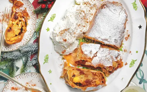 Delizioso strudel di mele con pasta sfoglia, cosparso di zucchero a velo e servito con panna montata e cannella.