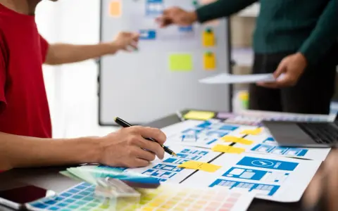 Zespół projektuje interfejsy, analizując potencjalne ux designer zarobki. Na stole makiety, palety kolorów i laptop.