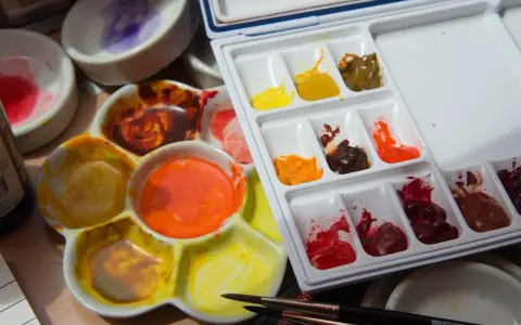 Palette d'aquarelles avec des couleurs vives, dont un mélange de **couleur jaune brun** dans un creux. Des pinceaux sont prêts à l'emploi.