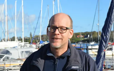 Mann mit Brille lächelt vor Segelbooten. Henningsen und Steckmest sind bereit für die nächste Ausfahrt.