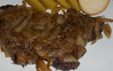 Pyszna kaszanka z patelni, duszona z cebulką, podana z ogórkiem kiszonym i kromką chleba.