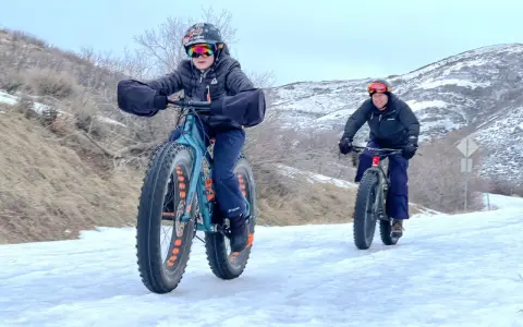 Two people ride fat tire bikes on a snowy path, demonstrating what are fat tire bikes for: tackling challenging winter terrain with their wide tires.