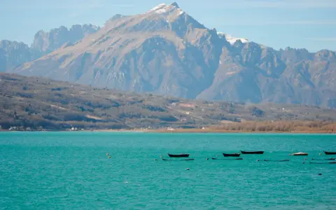 Boote treiben auf dem türkisfarbenen Lago di Santa Croce vor einer majestätischen Bergkulisse.