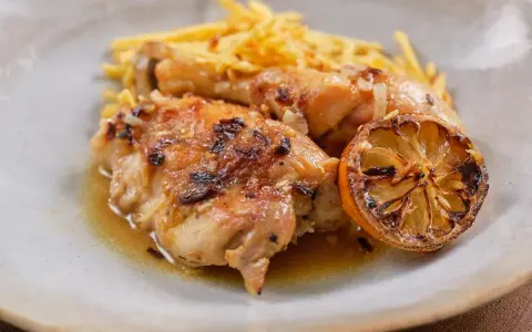 Delicioso pollo al limón con papas fritas crujientes y una rodaja de limón caramelizada.