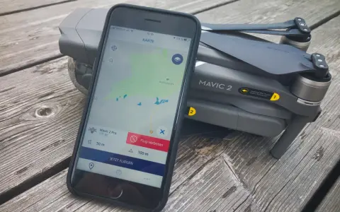 Eine Drohne liegt neben einem Smartphone, auf dem eine Drohnen-App mit Karte und Flugverboten angezeigt wird.