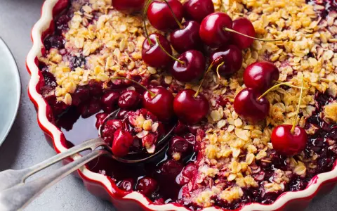 Delicioso postre con cerezas, cubierto de crumble dorado y adornado con cerezas frescas.