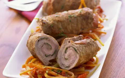 Drei köstliche kalbsrouladen italienisch auf einem Bett aus Gemüse. Eines ist aufgeschnitten und zeigt die saftige Füllung.