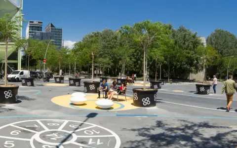 Barcelona autofrei: Menschen genießen einen grünen Platz mit Bäumen in großen Kübeln, Sitzgelegenheiten und einem Spielbereich auf dem Boden.
