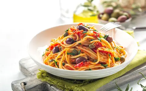 Un piatto invitante di spaghetti alla puttanesca, con olive nere, capperi e pomodoro, pronto per essere gustato.