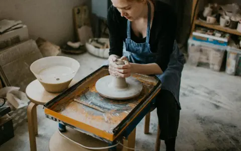 Jeune femme concentrée sur son apprentissage de l'artisanat de la poterie, façonnant l'argile sur un tour.