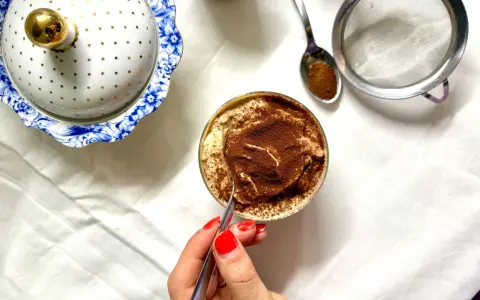 Deliziosa crema al caffè in bicchiere, cosparsa di cacao. Accanto, un elegante contenitore bianco e oro e un cucchiaino con cacao.