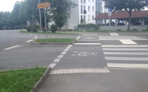 Ein Zebrastreifen mit Fahrradsymbolen auf dem Asphalt. Ein Schild weist in alle Richtungen.